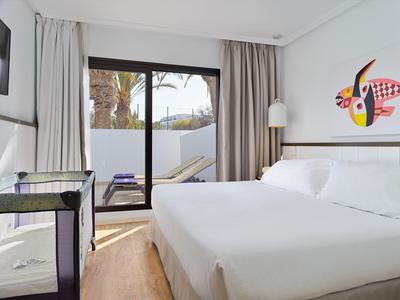 Camera d'hotel luminosa con letto king, scrivania in vetro e porta scorrevole verso patio.