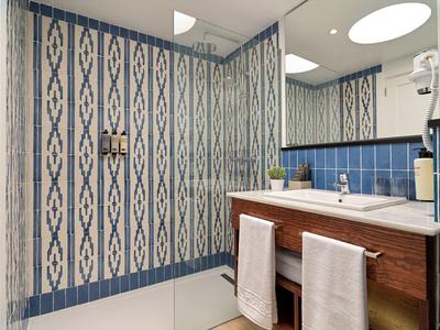 Bagno moderno con piastrelle blu e bianche a motivi, mobile lavabo in legno e due asciugamani bianchi.