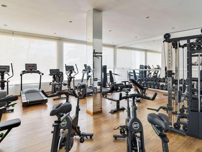 Bright gym with modern cardio and strength equipment, wooden floor, and large windows.