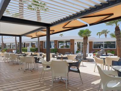 Modern hotel terrace with white tables and chairs under a curved canopy in daylight.