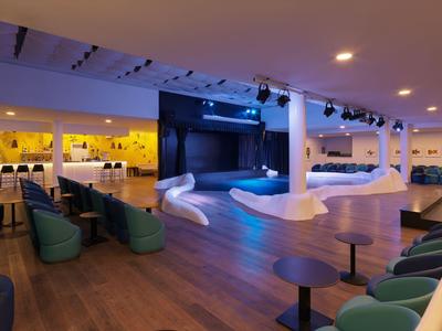 Modern hotel lounge with blue and yellow lighting, wooden floor, and seating areas.