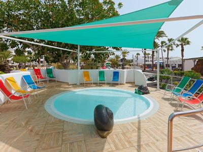 Round pool with colorful chairs and blue sun sails in a hotel setting.