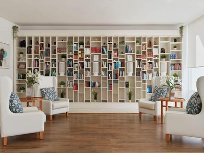 Moderner Wartebereich mit weißen Sesseln und großer Bücherwand in hellem Raum mit Holzboden.