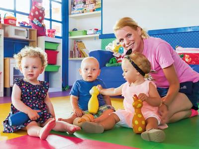 Donna con tre bambini seduti su tappeti colorati in una stanza giochi luminosa