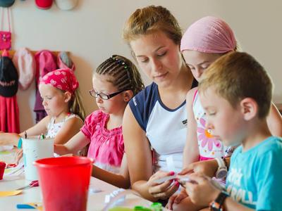 Un gruppo di bambini e una donna impegnati in lavori creativi a un tavolo al chiuso.