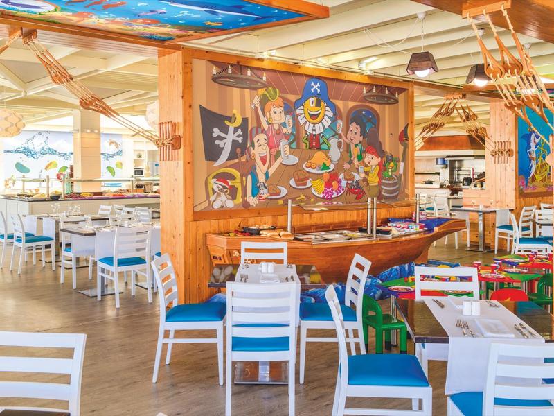 Ristorante luminoso a tema nautico con sedie bianche, cuscini blu e murale cartoon.