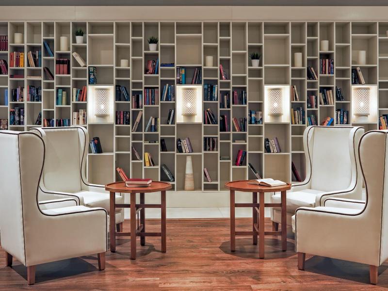 Area salotto simmetrica con poltrone bianche, tavoli in legno e una grande libreria a parete.