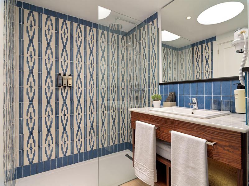 Bagno moderno con piastrelle blu e bianche a motivi, mobile lavabo in legno e due asciugamani bianchi.