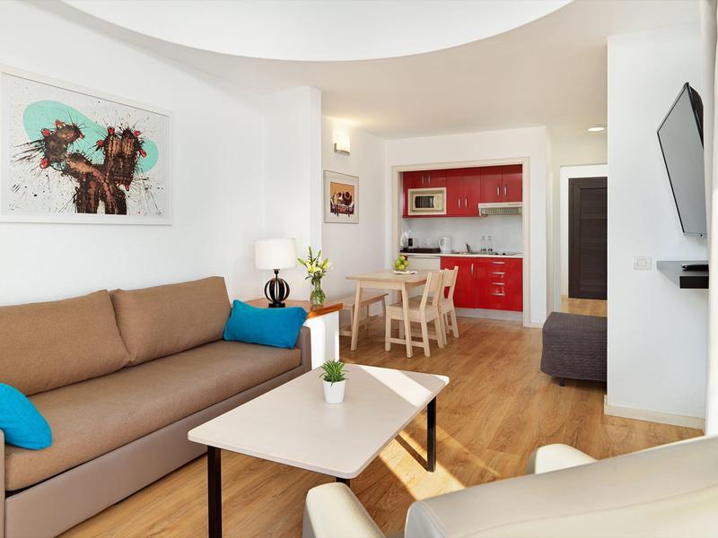 Soggiorno moderno con divano marrone, tavolino bianco e cucina rossa sullo sfondo