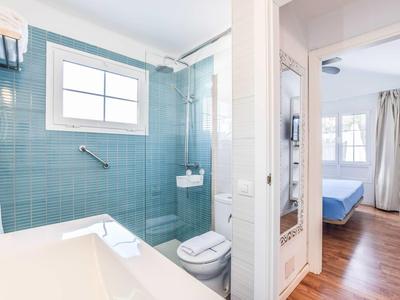 Helles Bad mit blauen Kacheln, Waschbecken, Toilette und Dusche, angrenzend an Schlafzimmer mit Holzfußboden.