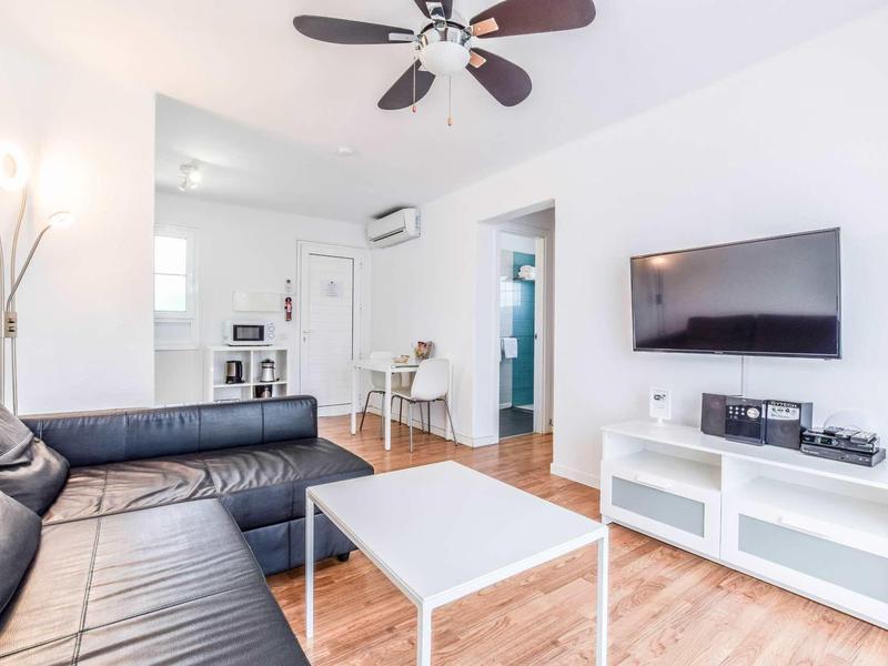 Helles Wohnzimmer mit schwarzem Ledersofa, weißem Couchtisch, Deckenventilator und Wand-TV.