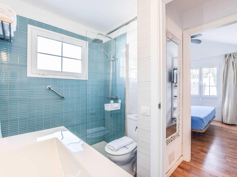 Helles Bad mit blauen Kacheln, Waschbecken, Toilette und Dusche, angrenzend an Schlafzimmer mit Holzfußboden.