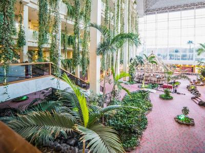 Großes Atrium mit vielen grünen Pflanzen, Palmen, roten Sitzbänken und bodentiefen Fenstern.