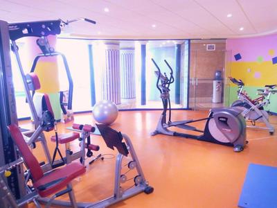 Moderner Fitnessraum mit orangem Boden, Trainingsgeräten und großem Fenster für Tageslicht.