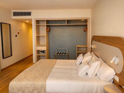 Hotelzimmer mit Doppelbett, Kissen, offenem Kleiderschrank und warmem Licht.