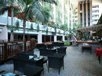 Außenbereich eines Cafés mit schwarzen Sitzmöbeln, Palmengärten und hohen Gebäuden im Hintergrund.