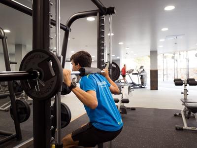 Hombre haciendo sentadillas con barra en un gimnasio iluminado.
