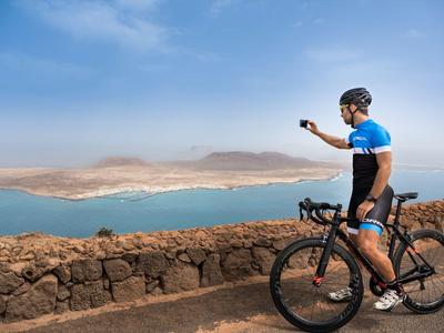Ciclista con casco toma una foto de un paisaje con agua y montañas.