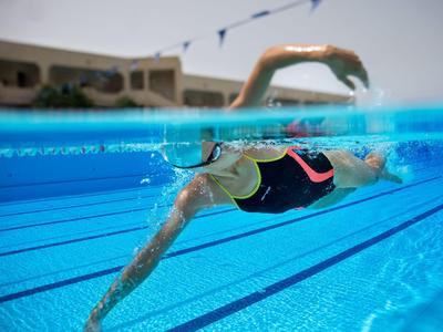 Mujer nadando en una piscina al aire libre clara con edificios al fondo.