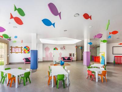 Kleurrijke, lichte kleuterklaslokaal met kleine tafels, stoelen en visdecoraties aan het plafond.