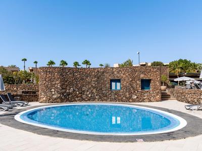 Rond zwembad met helder water voor een rustieke stenen muur en ligstoelen.