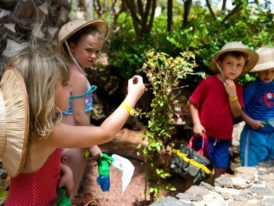 Kinderen verkennen de natuur buiten met hoeden en speelgoed in een zonnige tuin.