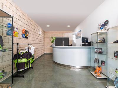 Área de recepción moderna con mostrador blanco, estantes y equipo deportivo en la pared.