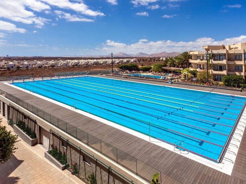 Groot buitenzwembad met banen naast hotelgebouwen en uitzicht op de stad.