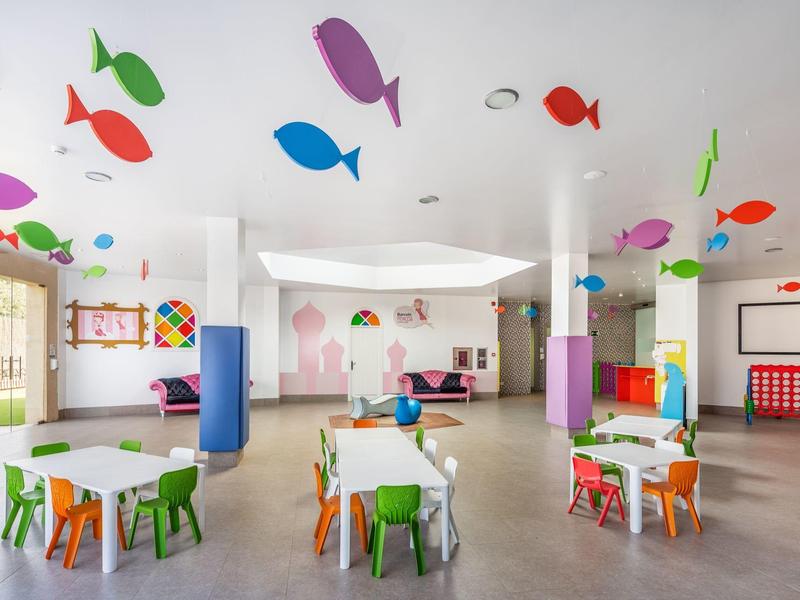 Kleurrijke, lichte kleuterklaslokaal met kleine tafels, stoelen en visdecoraties aan het plafond.