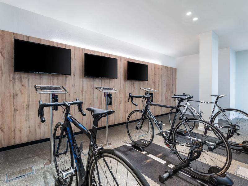 Moderne fitnessruimte met fietsen en drie aan de muur bevestigde schermen.