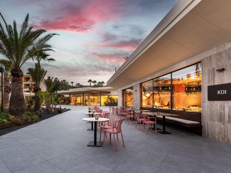 Moderne buitenruimte van een hotel met zitplaatsen en palmbomen bij zonsondergang.