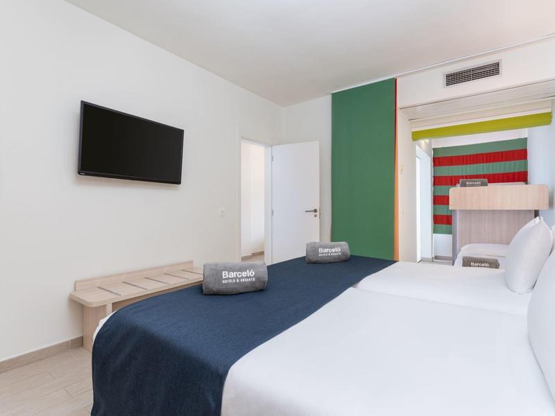 Moderne hotelkamer met tweepersoonsbed, wand-tv en kleurrijk wandontwerp op de achtergrond.