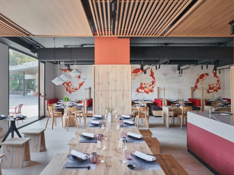 Modern interieur van een restaurant met houten tafels, banken en abstracte muurschilderingen.