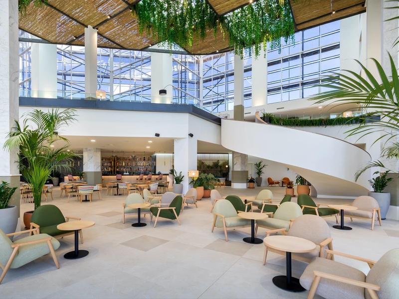 Lichte, moderne hotel-loungesectie met planten, zitgroepen en een witte wenteltrap.