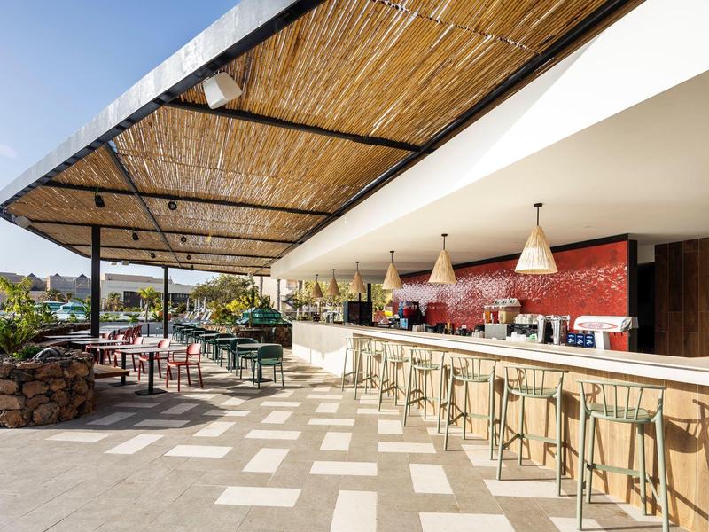 Moderne buitenbar met krukken en bamboedak op een zonnige dag.