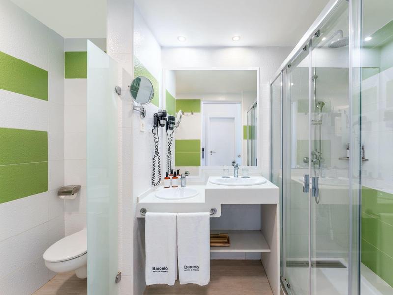 Moderne hotelbadkamer met douchecabine, wastafel en groene accenten op de muren.