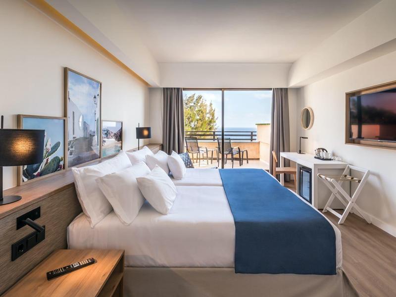 Moderne hotelkamer met tweepersoonsbed, balkon en zeezicht.