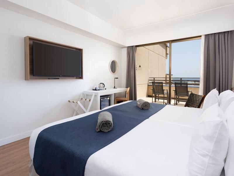 Moderne hotelkamer met tweepersoonsbed, balkon en zeezicht.