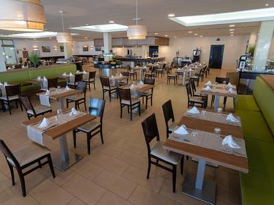 Spazio ristorante luminoso e moderno con tavoli apparecchiati e panchine verdi.