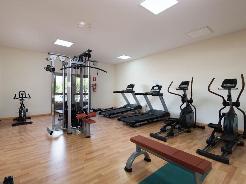 Palestra moderna con tapis roulant, ellittiche, cyclette e macchine per pesi su pavimento in legno.