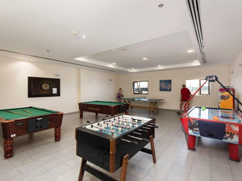 Sala giochi con tavoli da biliardo, calcio balilla, air hockey e freccette in uno spazio luminoso.