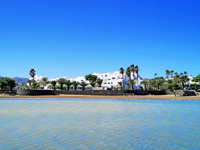 Resort con palme vicino a spiaggia tranquilla sotto cielo azzurro limpido