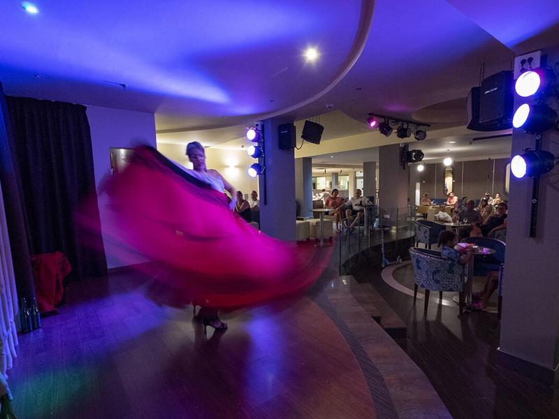 Un ballerino vibrante gira su un piccolo palco sotto luci blu e viola in un locale accogliente.