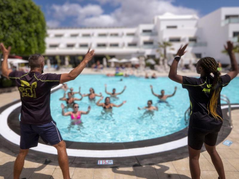 Due istruttori conducono una vivace sessione di esercizi in piscina con molti partecipanti in una piscina d'hotel.