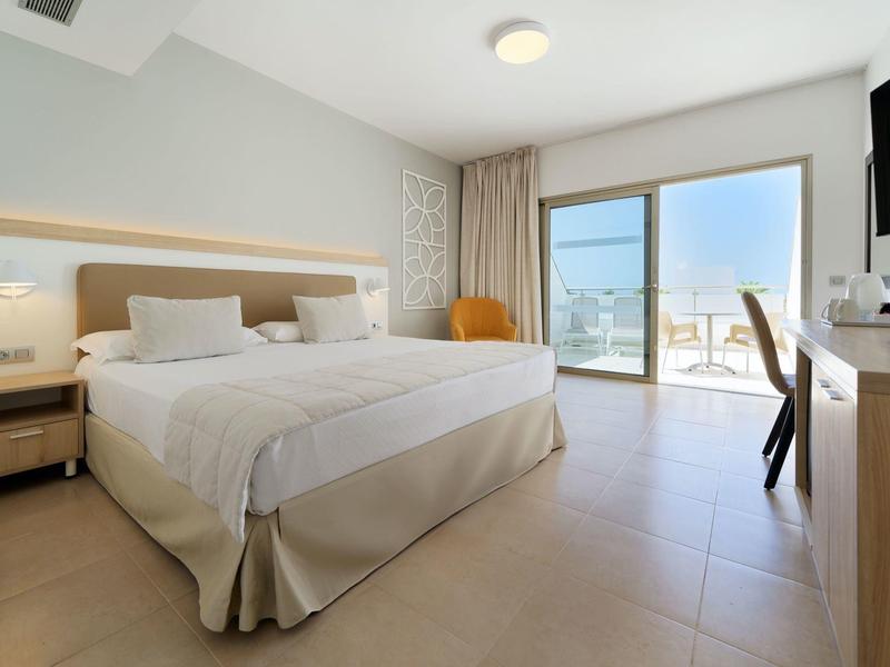 Camera d'hotel luminosa con letto matrimoniale, porta scorrevole verso il balcone e TV a muro.