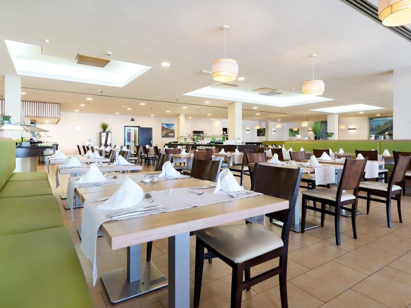 Ampia sala da pranzo dell'hotel con tavoli e sedie ordinati, illuminazione luminosa.