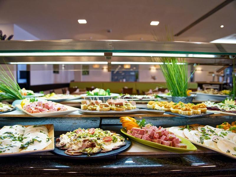 Buffet con vari antipasti, tra cui insalate, carni e pane, disposti su piatti.