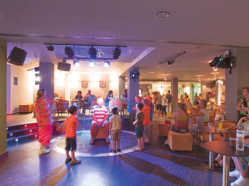 Area del palco interna con pubblico e bambini che ballano sotto una luce soffusa.