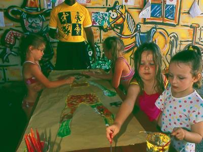 Kinder basteln an einem großen Tisch in einem farbenfrohen, mit Wandbildern dekorierten Raum.