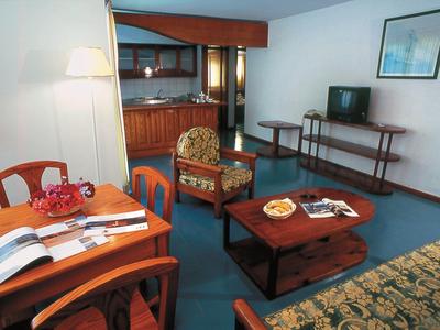 Wohnzimmer mit blauem Teppich, Holzmöbeln, Sessel, Tisch, Sofa und Stehlampe, hell und einladend.